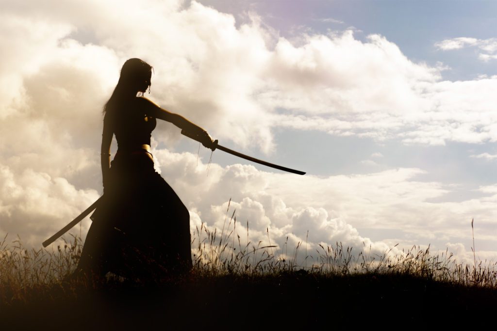 Silhouette of a woman warrior pointing with a samari sword.