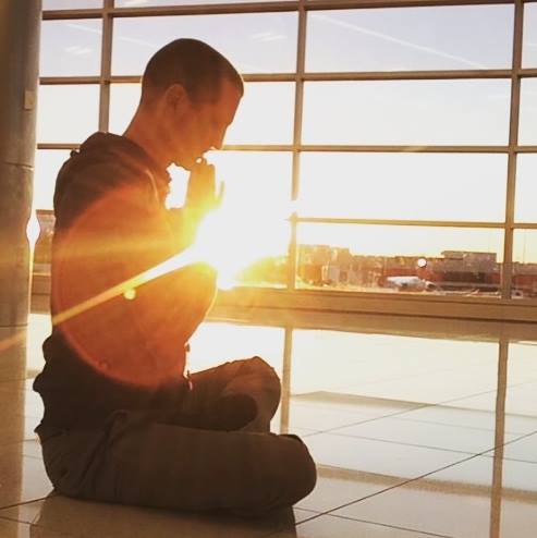 Man sitting on the floor meditating with the sun's shining behind him.