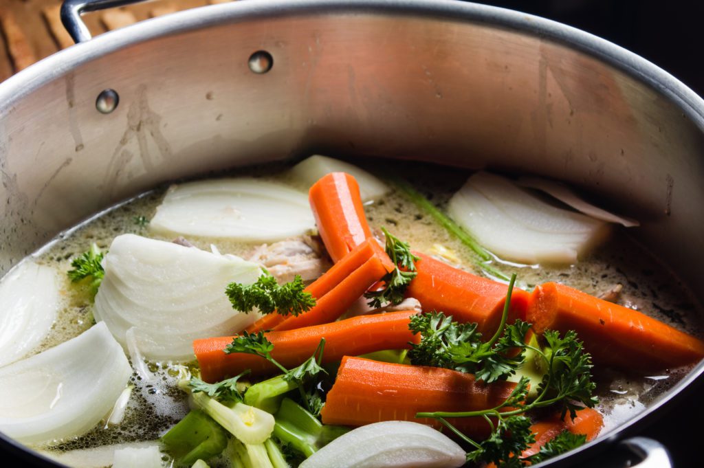 A big pot filled with chopped onion, carrot, celery, parsley and liquid.