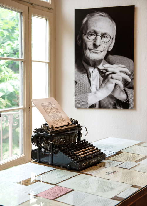 An old-fashion typewriter sits on a table with a collection of hand-written documents.