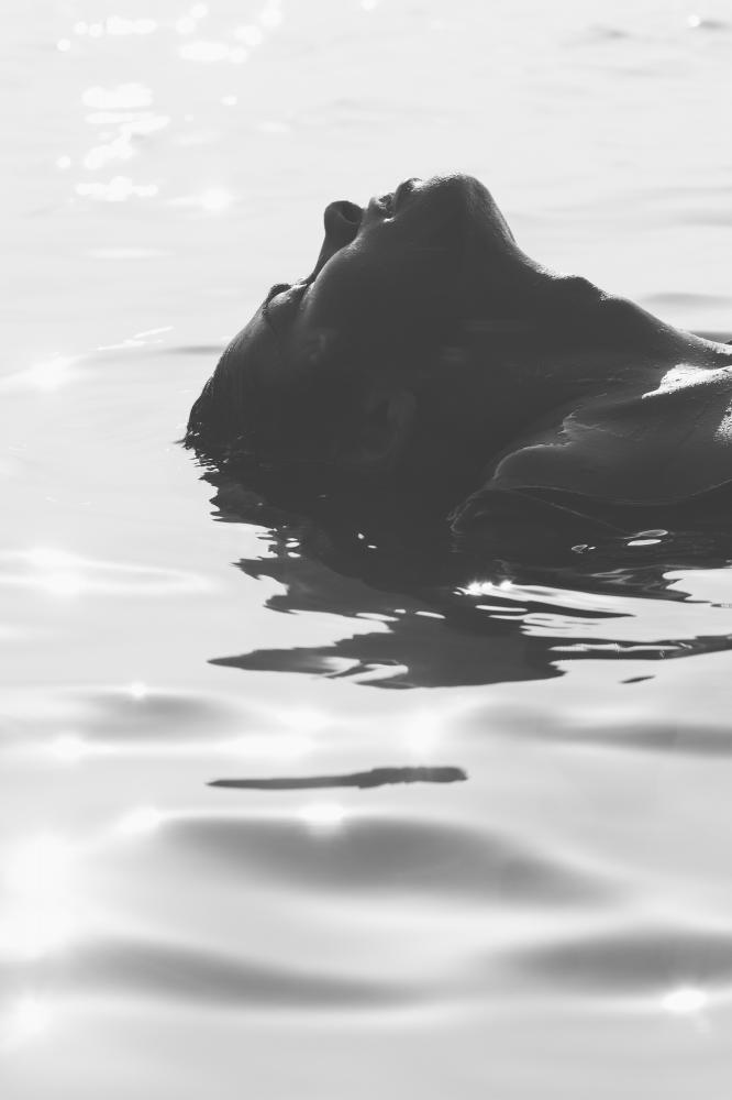 Black and white image of a woman floating in water with her head tilted back.