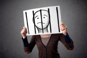 Person holding up an illustrated image of a face behind bars infront of their face.