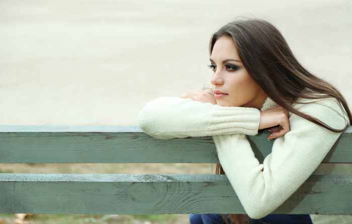 A young woman wearing a white sweater leans her arms on top of worn painted fence.