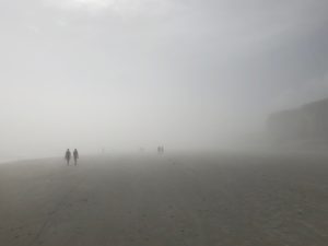 People walking on a large stretch of foggy beach.