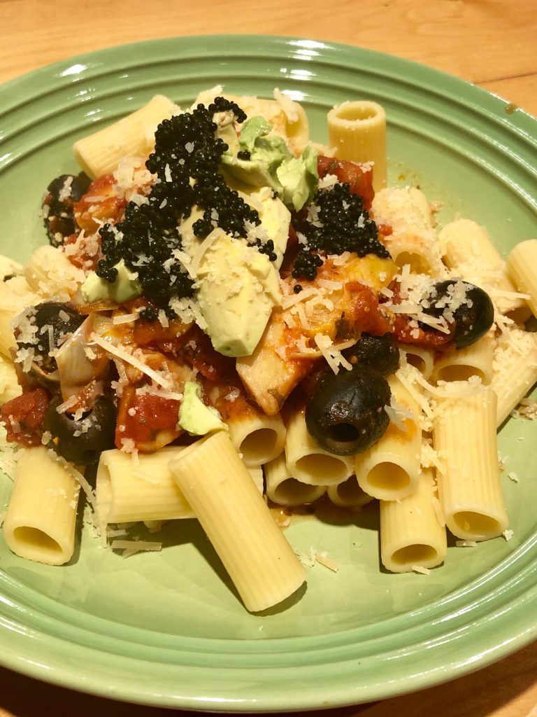 A plate of pasta topped with red sauce, cheese, avocado, black olives and caviar.