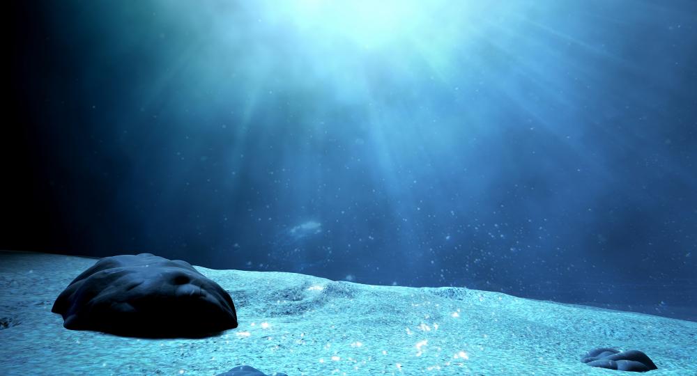 A large rock sits on a sun-lit, sandy ocean floor.