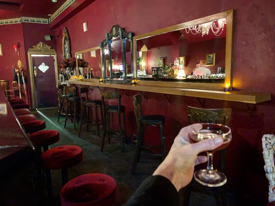 Hand raises a glass to an empty bar in a red room.