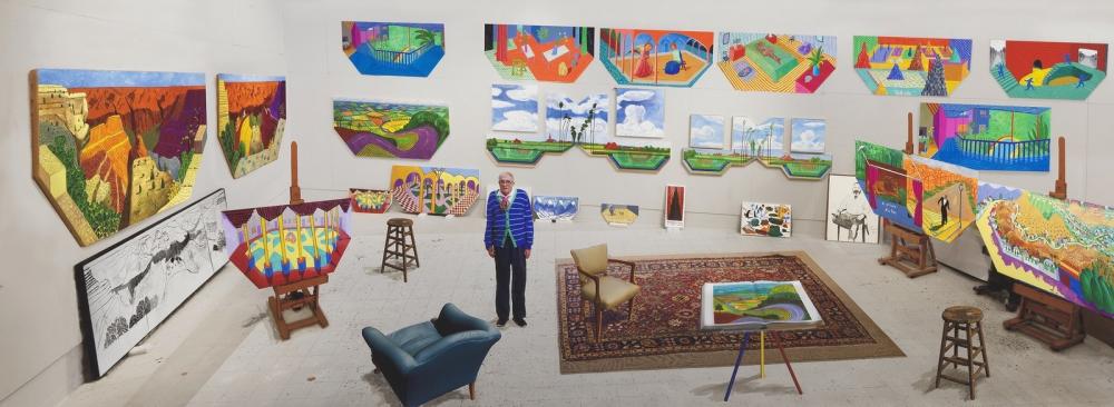 Artist David Hockney surrounded by art in a studio.