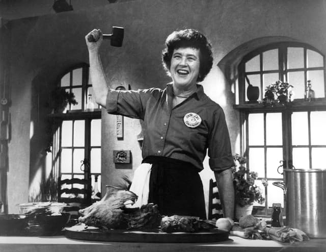 Black and white image of Julia Child raising a mallet in her right hand.