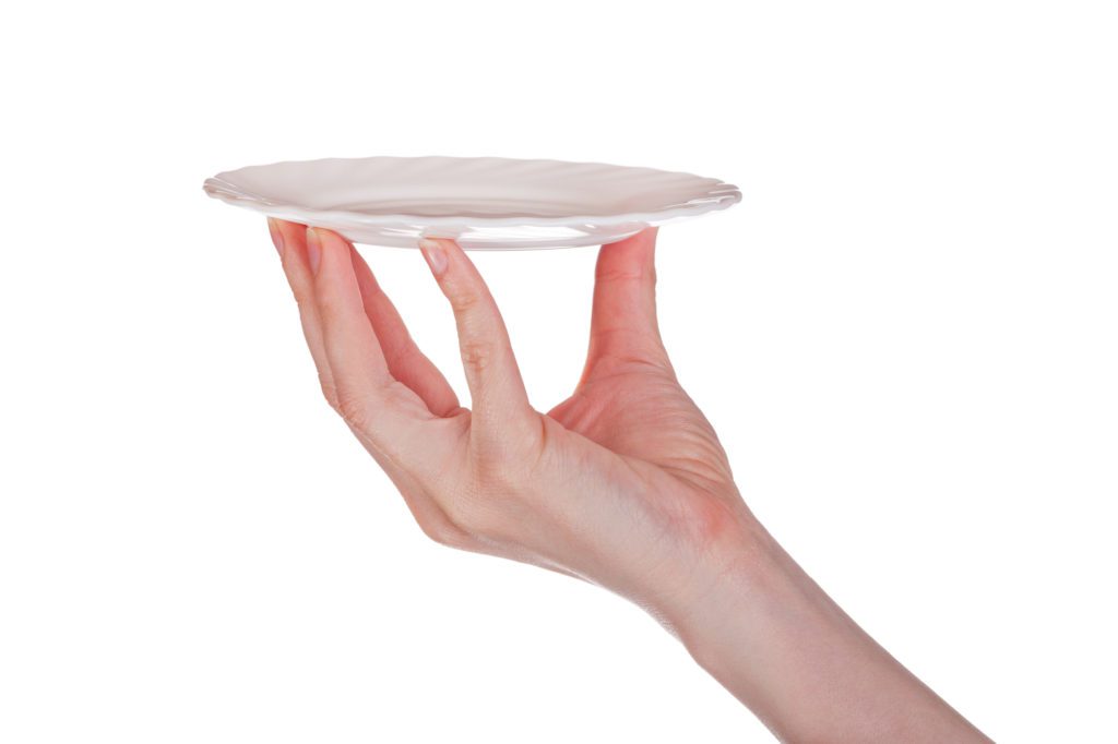 Fingers holding up a small white ceramic plate.