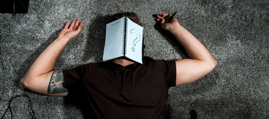 Person laying down with open notebook and a large question mark covering their face, symbolizing fear of judgment