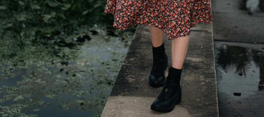 Person in floral skirt standing on the edge of a concrete wall with greenery on one side and a puddle on the other, symbolizing creative solutions