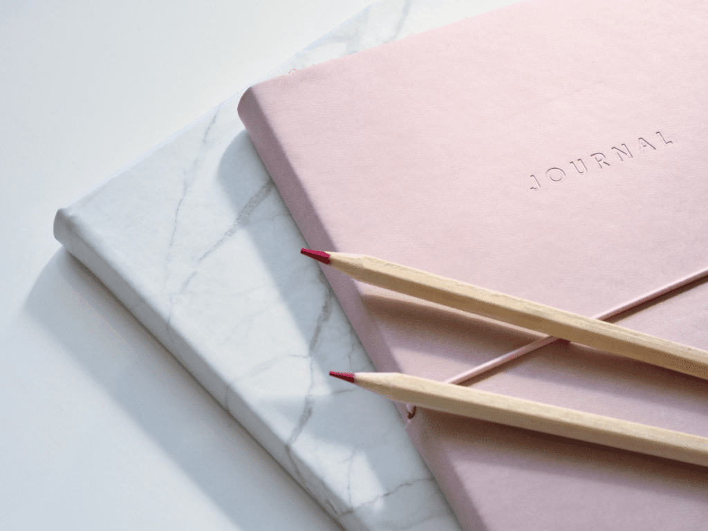 two journals, one marbled and one pink, and two pink pencils, symbolizing the tools it takes to live your dream