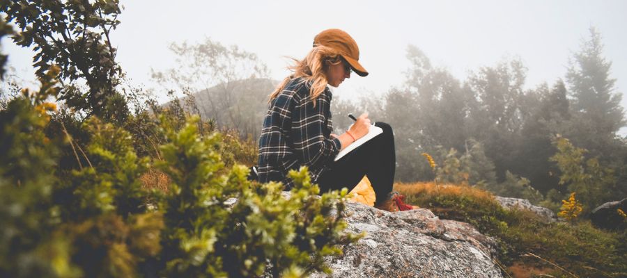 Girl journaling on a hill, in nature. Discovering the power of journaling