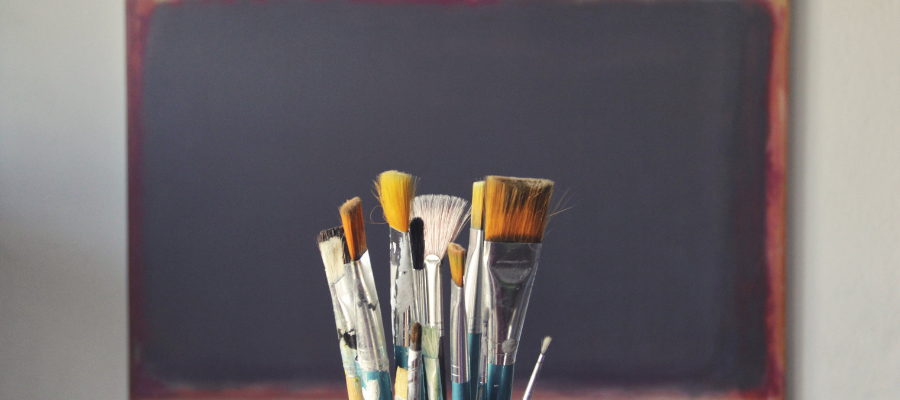 Up-close photo of paint brushes with an open canvas in the background, portraying the idea of investing in yourself by investing in a new creative project