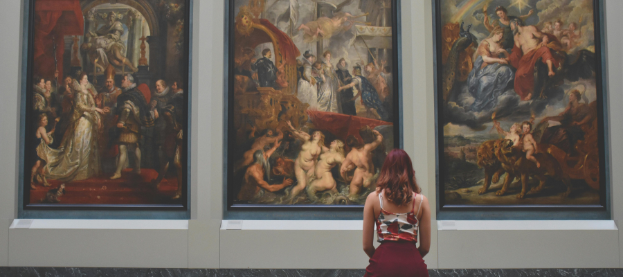 Photo from behind of a person, who appears to be young, sitting on a bench and observing art in a museum—a representation of making different retirement plans and living your retirement now.