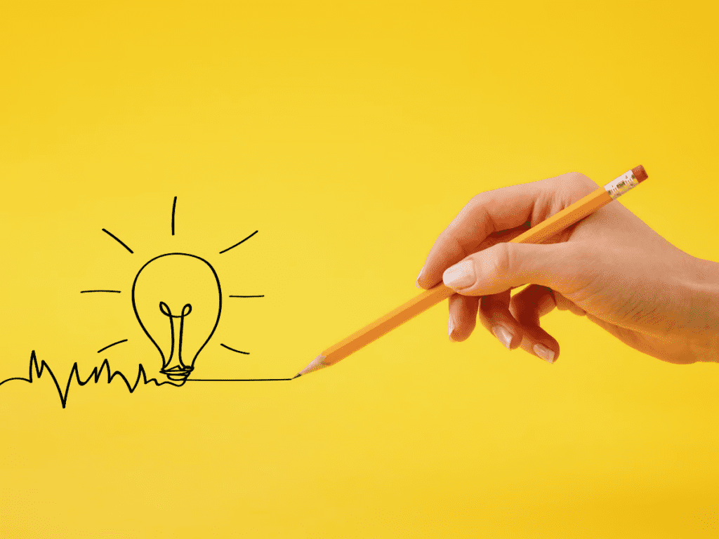 Bright yellow background with vector image of a hand holding a pencil and  with a hand-drawn light bulb trailing from the pencil—a representation of unlocking your big idea through truth-telling