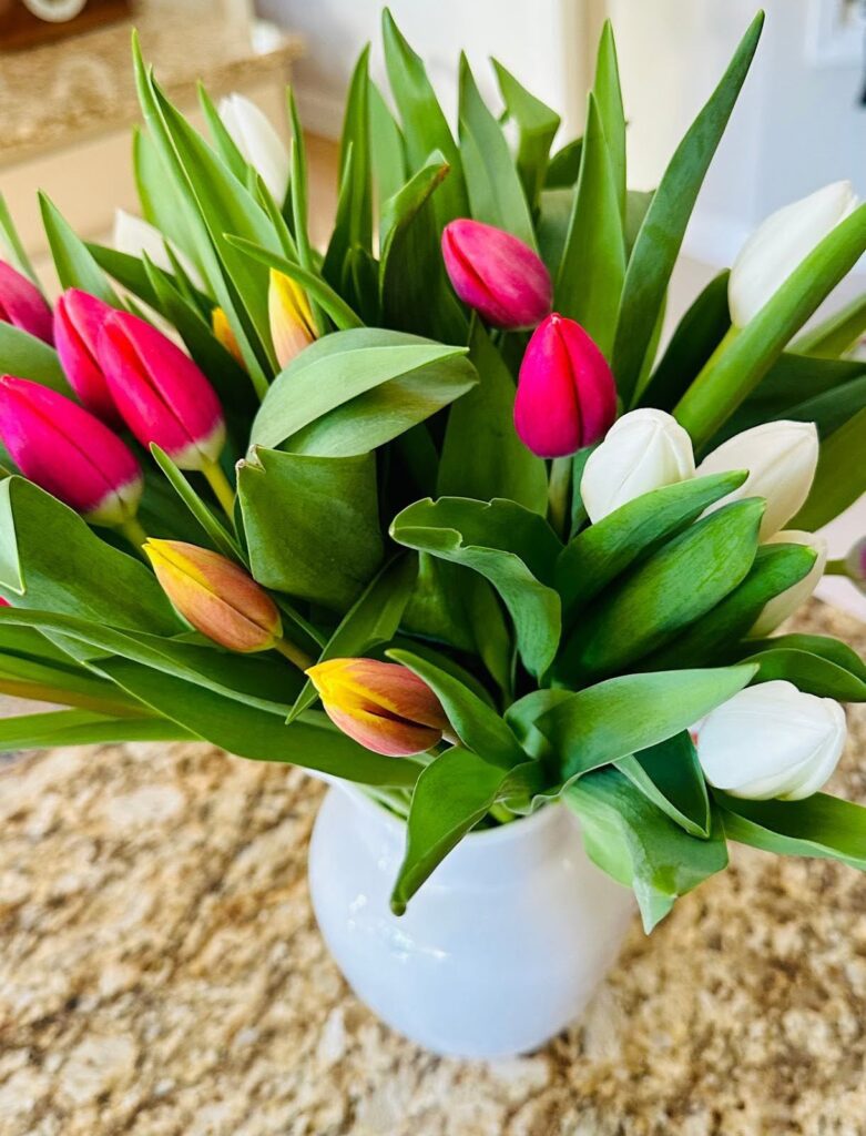 Beautiful pink, orange, and white tulips from the grocery store sit in a vase on a counter, and serve as an example of beauty that we can immerse ourselves in to feel better when we're burnt out. 