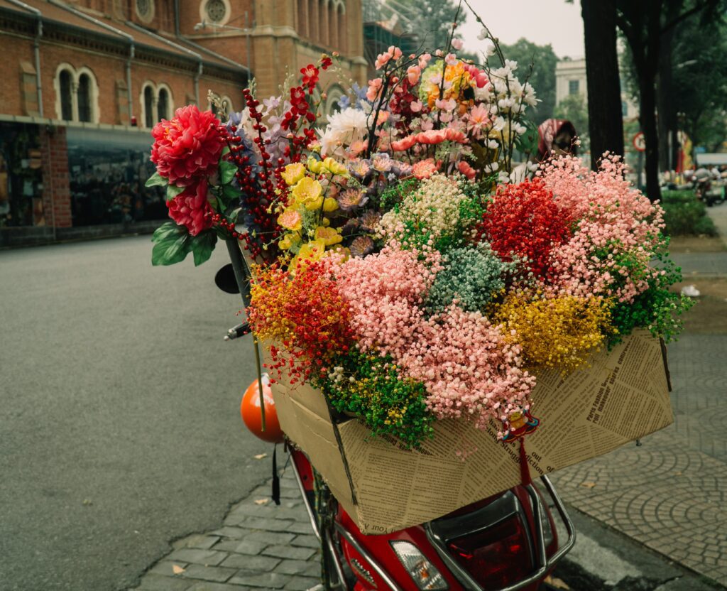 several bouquets with sprays of delicate pink, red, orange, and yellow flowers in the basket of a cherry red vespa parked on a street, to symbolize grasping your sense of wonder