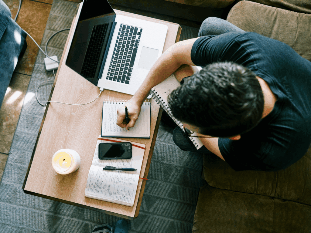 creative note-taking system; a man sits with several notebooks, a laptop, and a smartphone taking and organizing notes