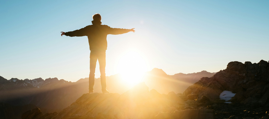 true self; a man standing on a mountaintop looking over a sunrise to represent coming home to your true self