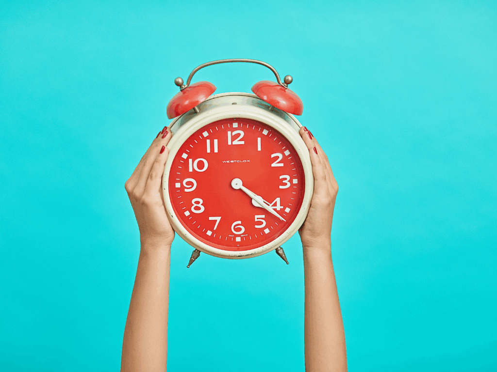 spend your time; a woman's hands holding a red alarm clock symbolize reflecting on how you spend your time
