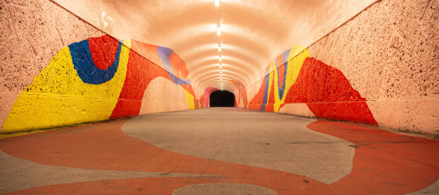 keep going; an underground lit pedestrian tunnel with abstract red, yellow, and blue paint along its walls ends in a dark opening to symbolize that we should keep going even when we can't see the outcome.