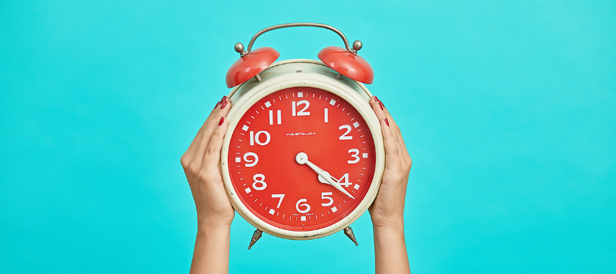 spend your time; a woman's hands holding a red alarm clock symbolize reflecting on how you spend your time