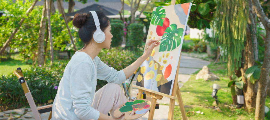 A woman sits in front of a painting of bright green and red leaves with headphones on, blocking out the noise around her, representing selective attention.
