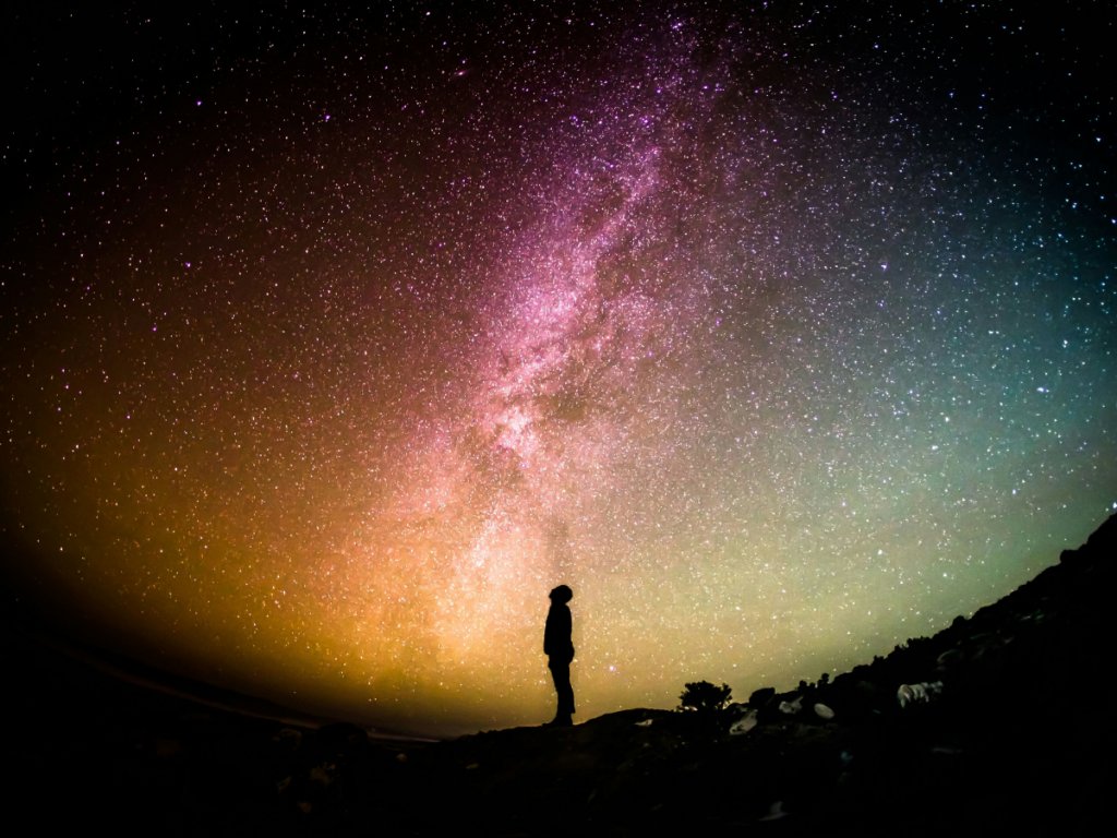 A photo of a person's silhouette looking up at the vast, colorful night sky full of stars illustrates the vivid beauty of the human experience.