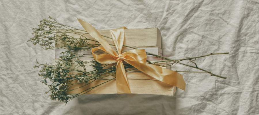 photo of paperback books, page side up, beautifully wrapped in gold ribbon with dried flowers.