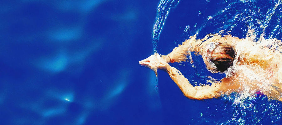 photo of a swimmer in beautiful blue water, making ripples as she swim breaststroke represent overcoming fear by going full send