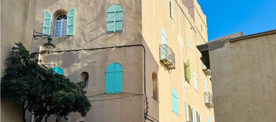 Portion of a photo by Susie deVille of Collioure, France, with particular attention to how the morning light touches some part of the tall, tan buildings, but leaves other parts in shadow.