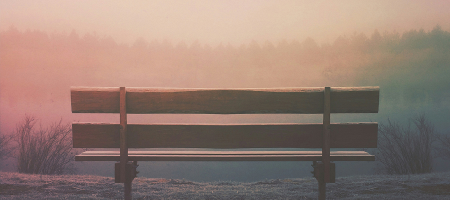photo of an empty park bench overlooking a pink tinged sky and a tree covered mountain represent the call for Sunday rest.